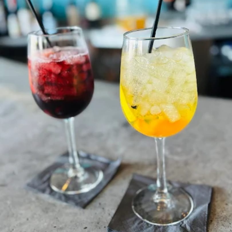 Two vibrant Comida cocktails, one red and one yellow, with ice and straws on a bar.