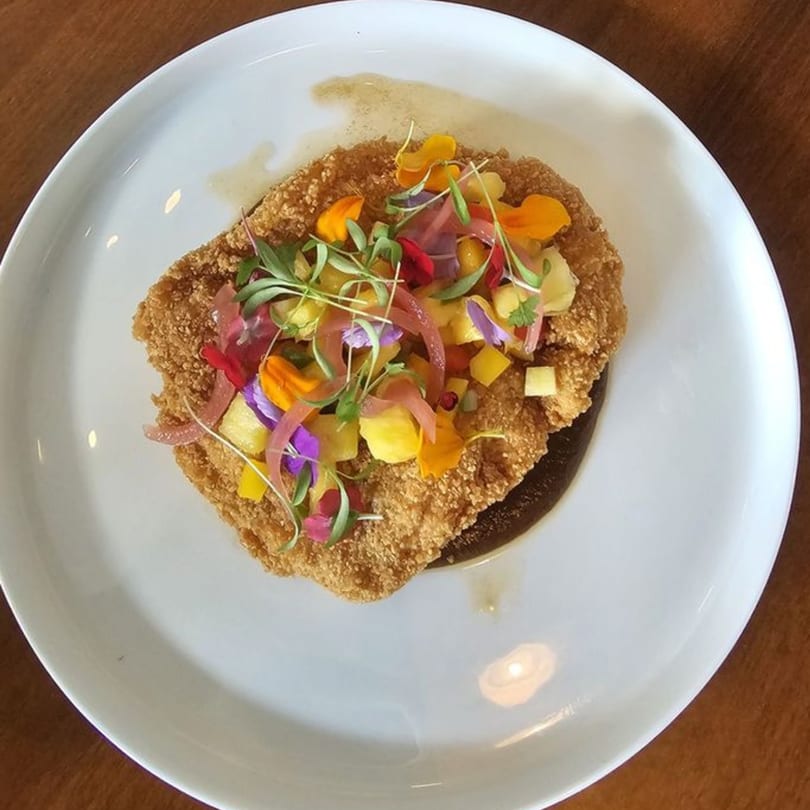 Comida's crispy fried chicken with colorful edible flowers, pickled onions, and mango on a white plate.