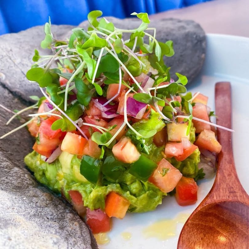 Comida's guacamole with diced tomatoes, red onions, green peppers, and microgreens, served with a wooden spoon.
