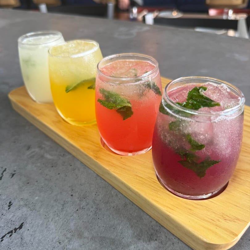 Four colorful Latin-American drinks with mint and ice on a wooden tray at Comida.
