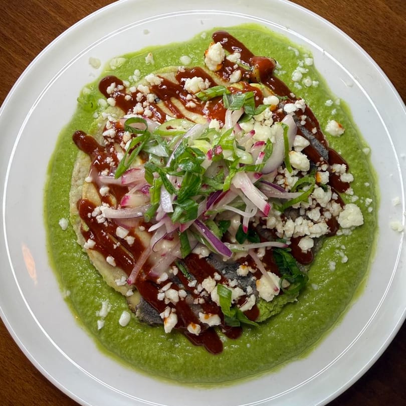 Comida's sopes with green sauce, red sauce, crumbled cheese, and sliced onions on a white plate.