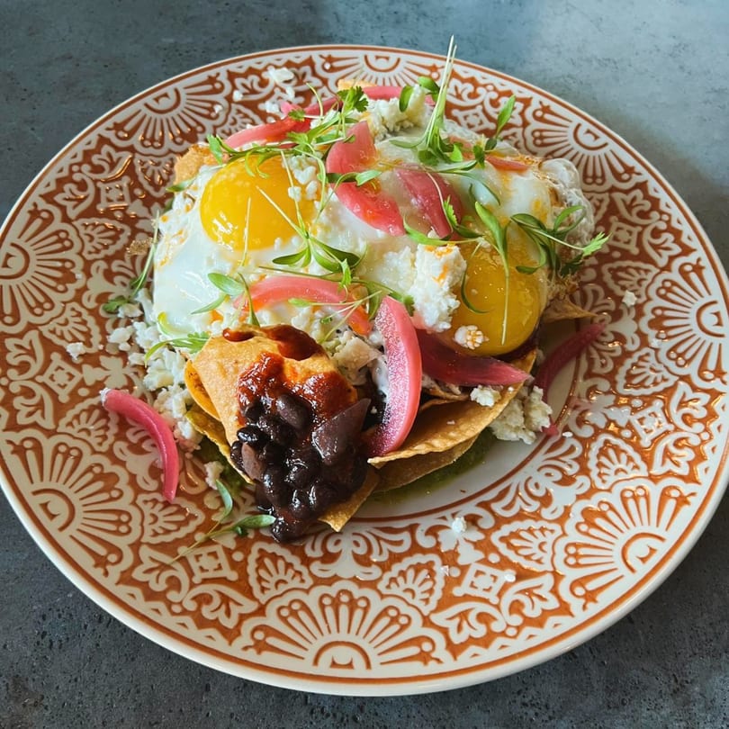 Comida's huevos rancheros with fried eggs, black beans, pickled onions, and microgreens on a patterned plate.